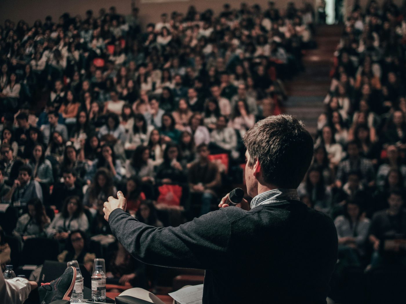 A speaker on stage facing a packed auditorium.