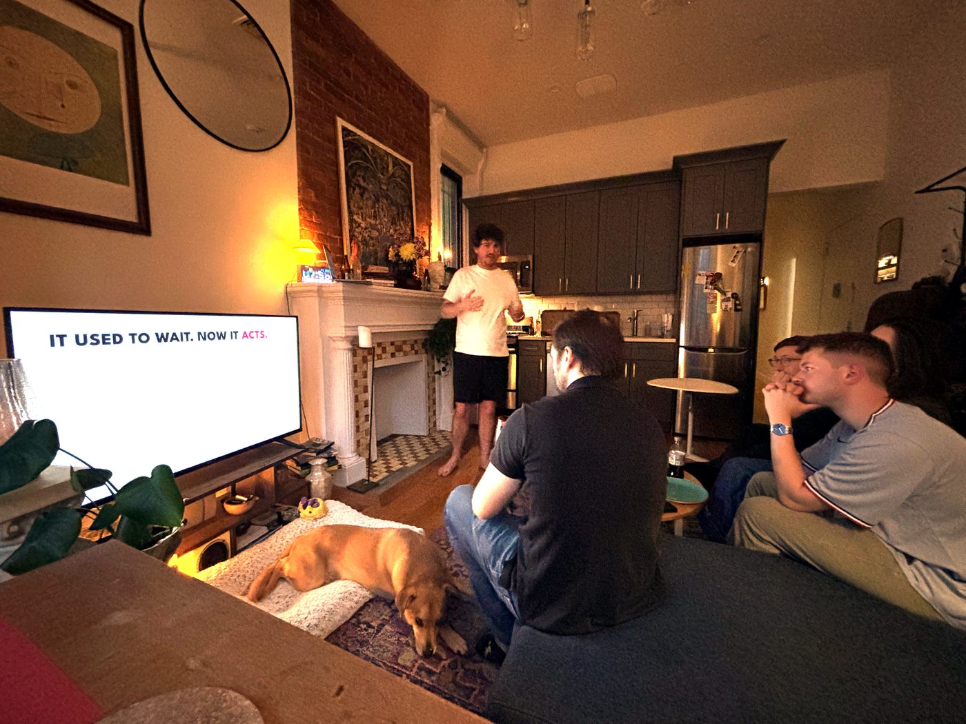 People sitting together in a living room, watching a presentation on a television.